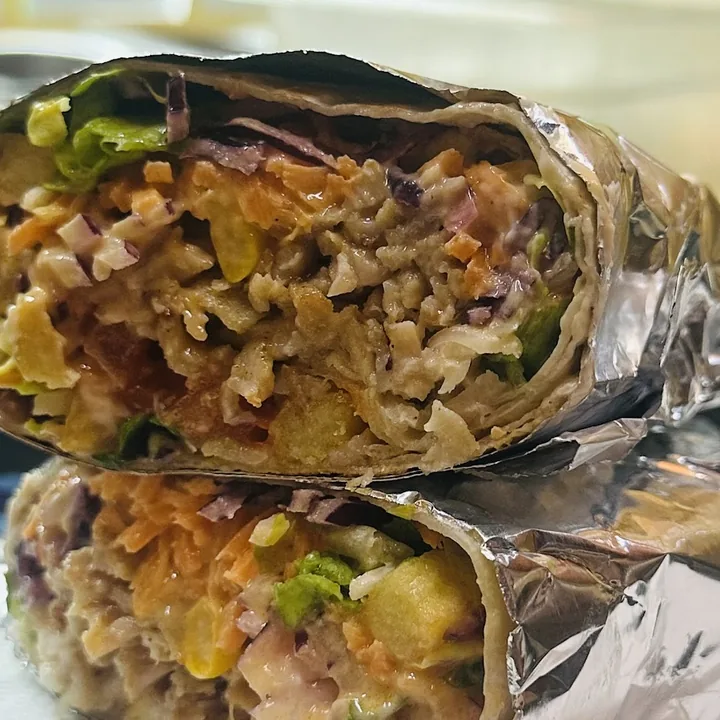 Piadina kebab tagliata a metà: carne, cavolo rosso, carote, patatine e salsa, avvolta nella carta stagnola.