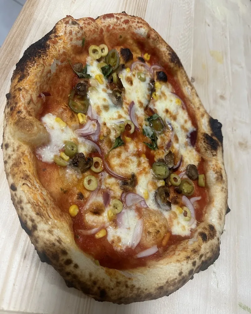 Pizza appena sfornata sulla pala di legno, con olive verdi, funghi, cipolla rossa, mais e mozzarella.