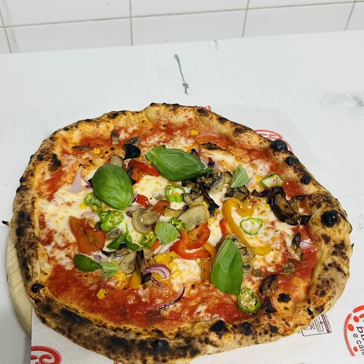 Pizza con peperoni, melanzane, funghi, cipolla e basilico fresco, sulla pala appena sfornata.